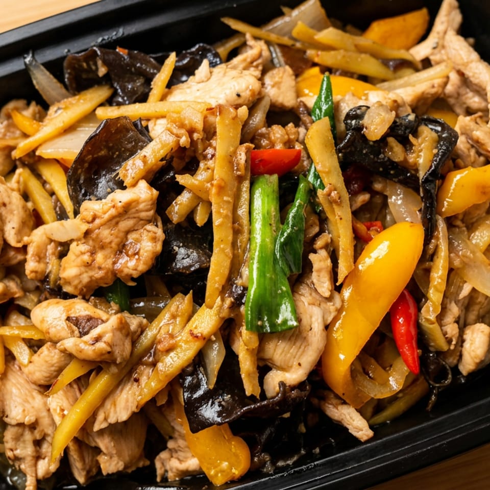 Stir-fried chicken with bamboo shoots, wood ear mushrooms, bell peppers, and onions in a black container.